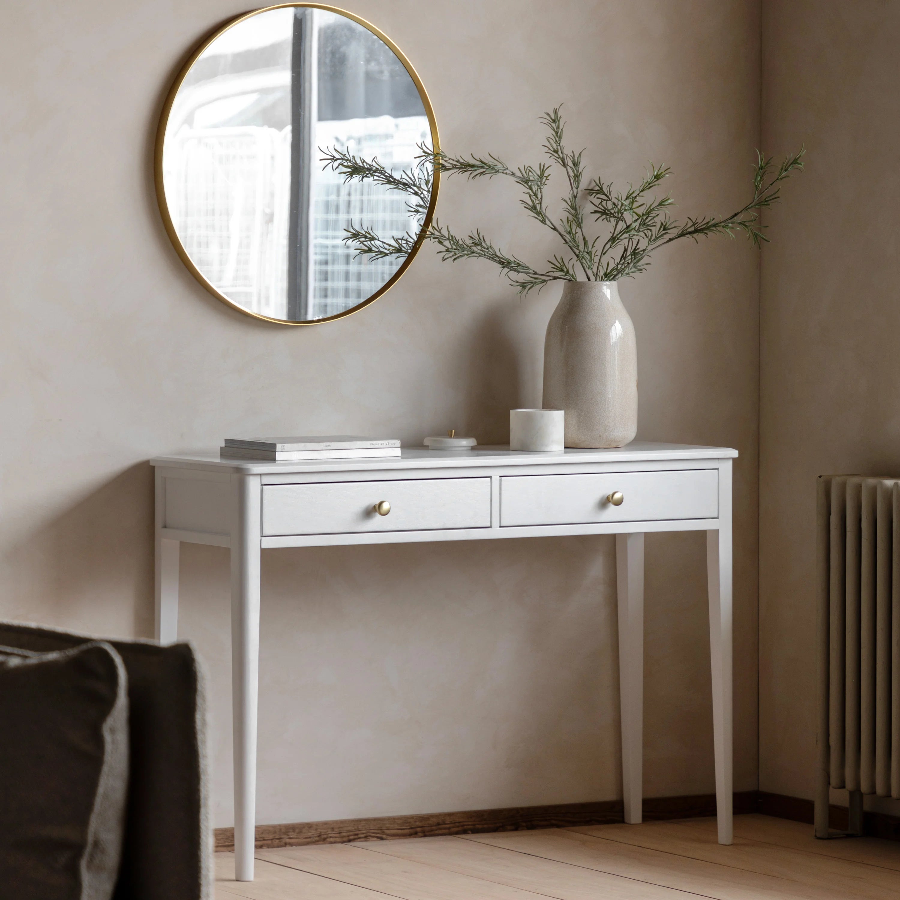 White console table with a round mirror, vase, and books against a beige wall.