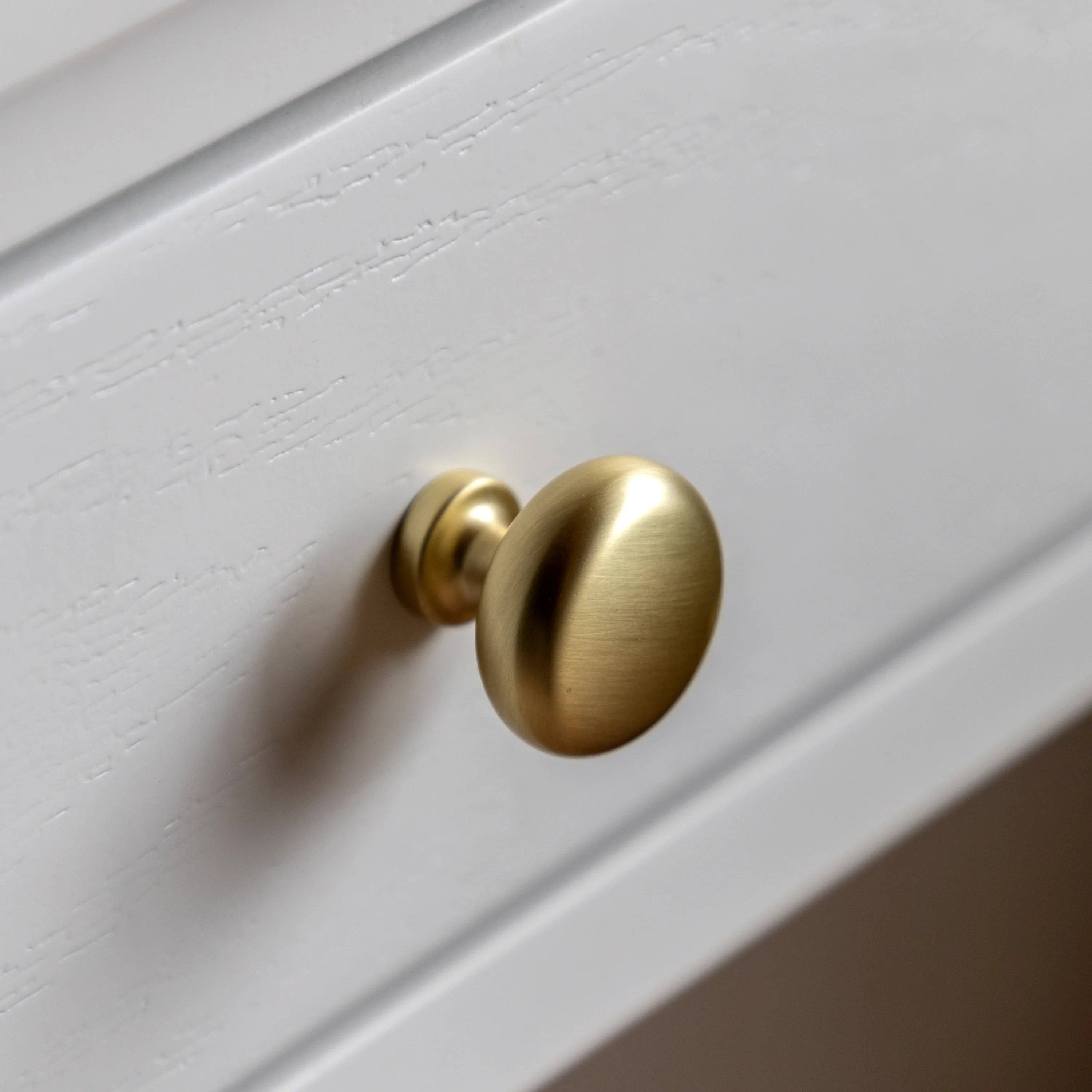 Gold cabinet knob on a white wooden surface